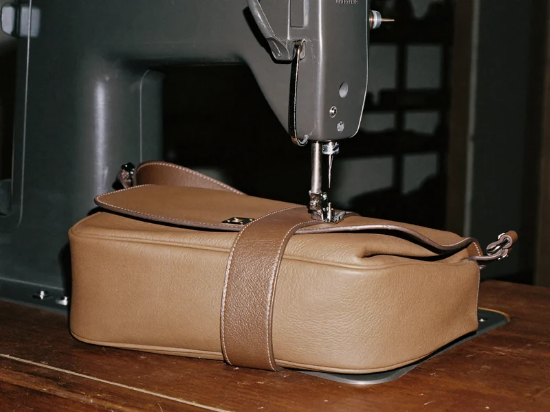 Illustration: Kräftige Nähmaschine setzt einen neuen Lederriemen an eine hellbraune Handtasche